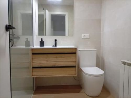 Baño moderno en Apartamentos La Machacona con tocador de madera, espejo, inodoro y paredes con azulejos blancos