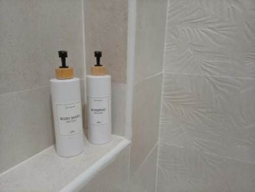 Dos botellas dispensadoras blancas con tapones de madera en estantería de baño de Apartamentos La Machacona, Cáceres