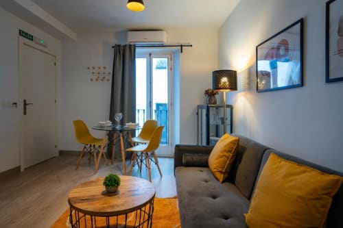 Apartamento moderno de 1 dormitorio en Cáceres con sofá gris, detalles amarillos, mesa de comedor y acceso a balcón en Apartamentos La