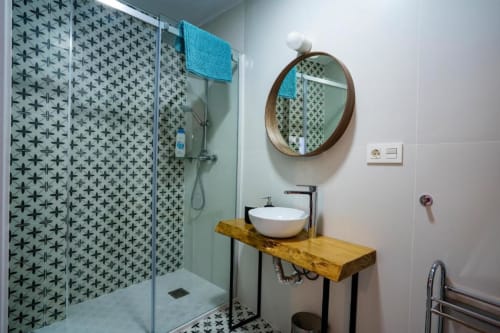 Baño moderno en apartamento de Cáceres con ducha de azulejos estampados, tocador de madera y espejo redondo