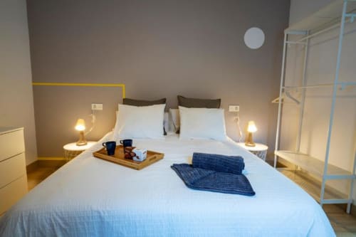 Dormitorio moderno en Apartamentos La Machacona de Cáceres con cama queen, ropa de cama blanca, lámparas gemelas y decoración contemporánea