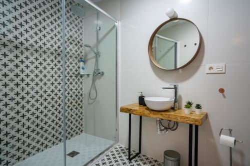 Baño moderno en Apartamentos La Machacona con ducha de azulejos decorativos, espejo redondo, tocador de madera y lavamanos blanco