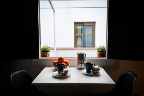 Desayuno con café, pasteles y naranjas sobre mesa blanca frente a ventana con vista al patio de Cáceres en La Machacona