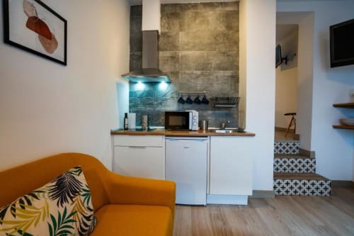 Sofá naranja con cojines estampados y cocina compacta con iluminación azul en apartamento de Cáceres