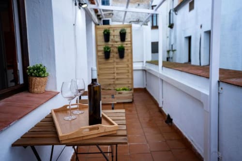 Terraza con muebles de madera, botellas de vino, copas y plantas en macetas en Apartamentos La Machacona en Cáceres