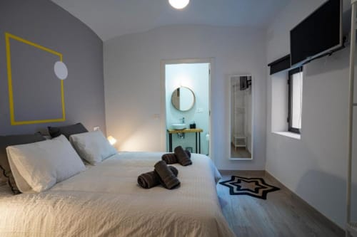 Dormitorio moderno en Apartamentos La Machacona, Cáceres, con cama doble, arte mural amarillo, baño privado y pantalla plana