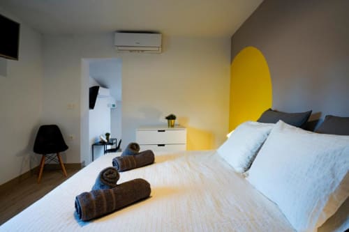 Dormitorio moderno en Apartamentos La Machacona en Cáceres con cama, pared amarilla, cajones blancos, silla negra y aire acondicionado