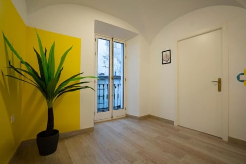 Sala de estar moderna en La Machacona Cáceres con pared acentuada amarilla, planta en maceta, pisos de madera y puertas al balcón