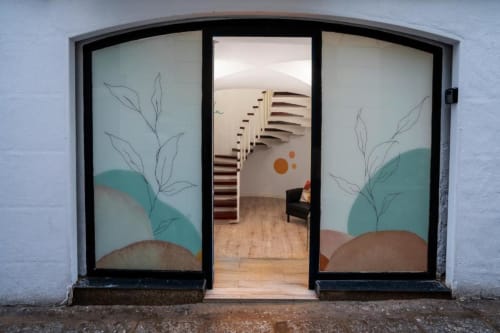 Entrada del apartamento en hotel La Machacona en Cáceres con puertas de vidrio artístico que abren a una moderna escalera de caracol y