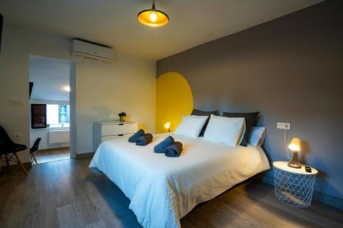 Dormitorio moderno en apartamento de Cáceres con cama blanca, cabecera amarilla, lámpara colgante y aire acondicionado