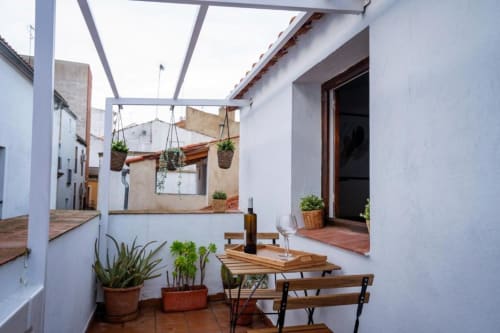 Zona de descanso en la terraza de Apartamentos La Machacona en Cáceres con bancos de madera, plantas en macetas y pérgola