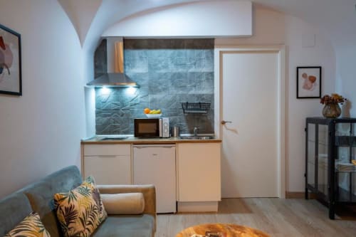 Cocina moderna en apartamento de Cáceres con azulejos azules, muebles de madera clara y zona de estar con sofá