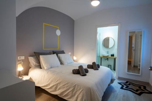 Dormitorio moderno en Apartamentos La Machacona en Cáceres con ropa de cama blanca, marco amarillo y baño privado