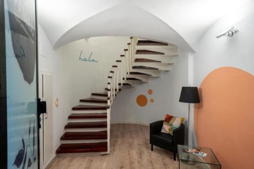 Escalera de caracol moderna en apartamento de Cáceres con paredes blancas, peldaños de madera oscura y mobiliario contemporáneo