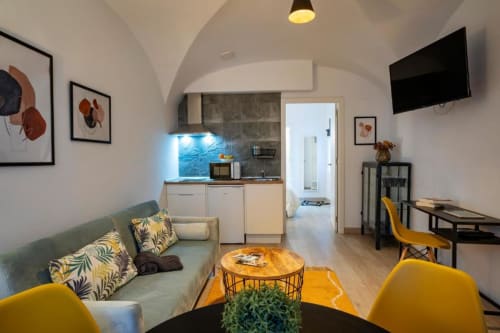 Moderno estudio en Cáceres con sofá verde, cocina americana, sillas amarillas y techo abovedado