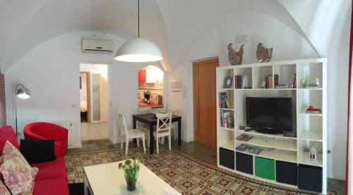 Moderno apartamento en planta baja en Cáceres con asientos rojos, mueble blanco con TV, zona de comedor y decoración