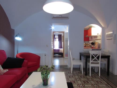 Moderno salón de apartamento en Cáceres con sofá rojo, lámpara de techo blanca, comedor y vista a la cocina