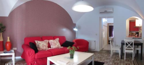 Sofá rojo moderno con pared a cuadros en apartamento La Machacona, Cáceres, con área de comedor y cocina visible