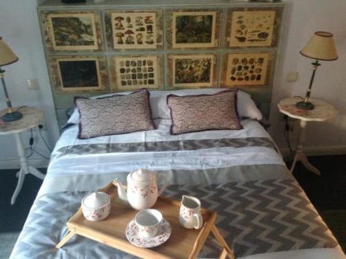 Acogedora habitación en Apartamentos La Machacona con cama, cojines decorativos, servicio de té en bandeja e láminas botánicas vintage