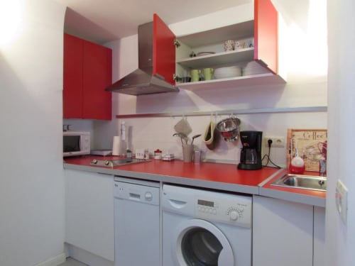 Cocina moderna con encimera roja, armarios blancos y electrodomésticos integrados en el apartamento La Machacona en Cáceres