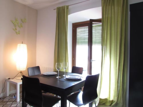 Comedor moderno en apartamento de Cáceres con mesa negra, vistas a la ciudad a través de puertas de cristal y cortinas verdes