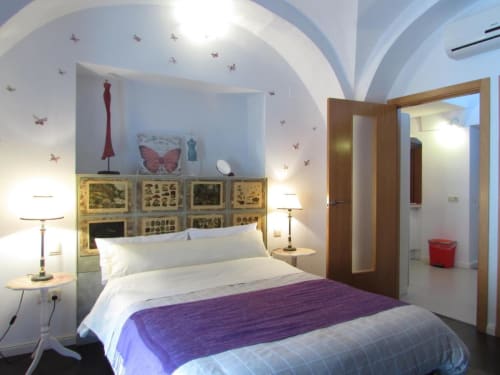 Dormitorio luminoso en apartamento de Cáceres con acento morado, cabecero decorado, techos abovedados, arte mural de mariposas y baño ensuite
