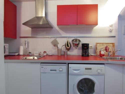 Cocina moderna con muebles rojos, lavavajillas, lavadora y electrodomésticos de acero inoxidable en apartamento de Cáceres