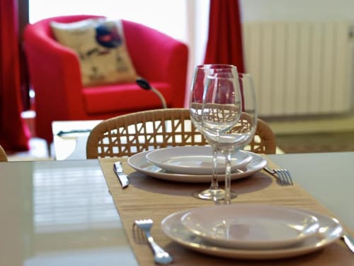 Mesa de comedor elegante con cubiertos, copas de vino y sillas de mimbre en el apartamento La Machacona, Cáceres