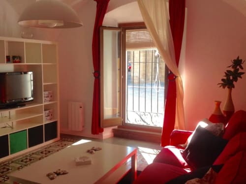 Luminoso salón moderno con sofá rojo, televisor y vistas al balcón en Cáceres