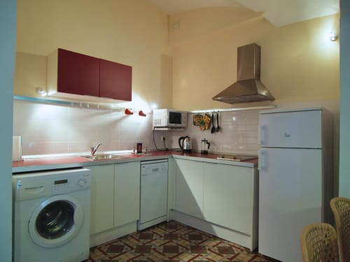 Cocina moderna de Apartamentos La Machacona con muebles blancos, encimera roja, electrodomésticos de acero inoxidable y detalles burdeos