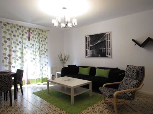 Sala moderna de Apartamentos La Machacona con sofá negro, detalles verdes y mobiliario contemporáneo