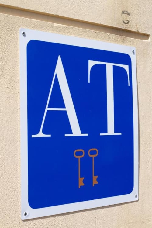 Señalética vintage azul de metal 'ATI' con llaves decorativas en pared beige en Apartamentos La Machacona, Cáceres