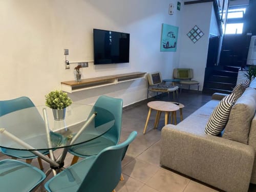 Salón moderno en apartamento de Cáceres con asientos en color verde azulado, televisor de pantalla plana, sofá y comedor con vistas a la ciudad