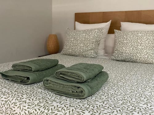 Dormitorio de Apartamentos La Machacona con toallas verdes dobladas en la cama, ropa de cama estampada, cabecero de madera y lámpara tejida