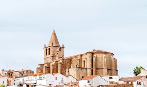 Iglesia histórica de piedra con torre dominando los edificios blancos del pueblo en España, cerca de Apartamentos La Machacona