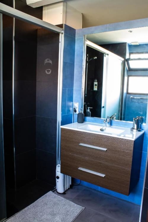 Baño moderno en apartamento de Cáceres con azulejos azules, ducha abierta, mueble de madera y espejo