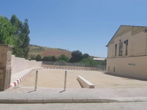 Zona de aparcamiento de Apartamentos La Machacona en Cáceres con bordillos rayados, bolardos y edificio beige