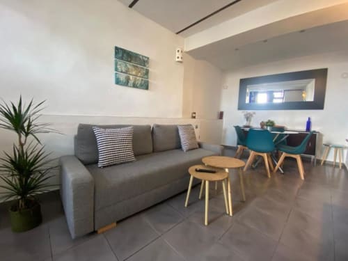 Sala de estar moderna en Apartamentos La Machacona en Cáceres con sofá gris, mesas de madera y zona de comedor