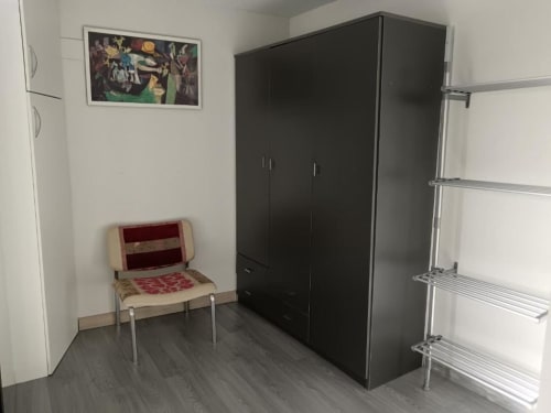 Apartamento de 1 dormitorio en Cáceres con armario oscuro, estantería metálica, silla roja y suelo de baldosas