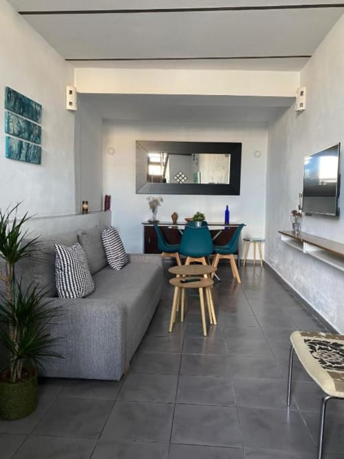 Moderno apartamento de 1 dormitorio en Cáceres con sofá gris, sillas de comedor verde azulado y vistas de monumentos locales