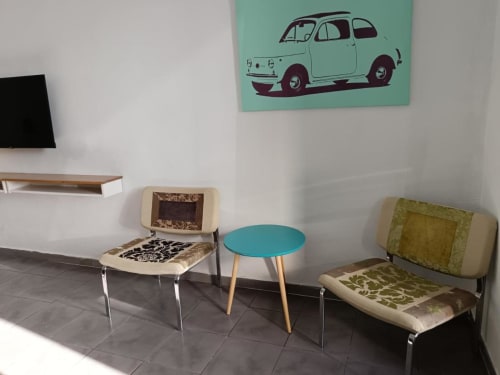 Zona de estar retro en Apartamentos La Machacona con sillas vintage, mesa turquesa y arte clásico de autos sobre menta