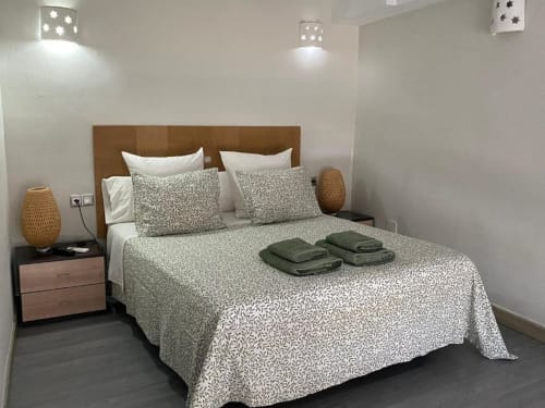 Moderno dormitorio en Apartamentos La Machacona de Cáceres con cabecero marrón, ropa de cama estampada, toallas verdes y textiles tejidos