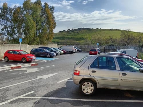 Estacionamiento de Apartamentos La Machacona en Cáceres con varios vehículos y vista de colinas verdes