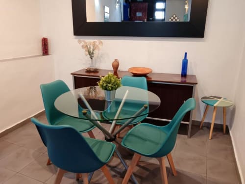 Comedor moderno en apartamento de Cáceres con sillas turquesas, mesa redonda de cristal y aparador de madera con decoración