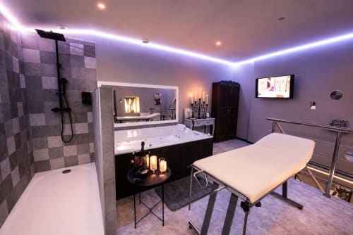 Suite spa luxueuse aux lumières ambiantes violettes, baignoire balnéo, douche pluie, lit de massage aux Secrets de Winna
