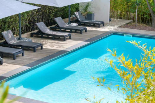 Villa Annette B&B resort pool with turquoise water, lounge chairs, umbrellas, and lush green backdrop in France
