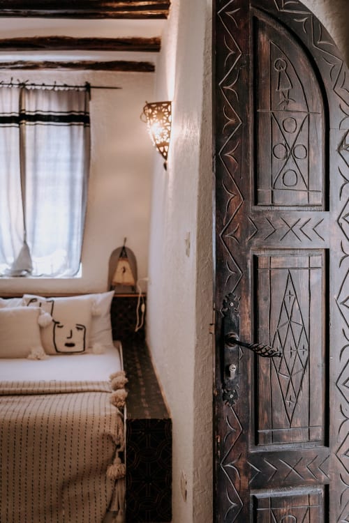 Porte en bois ouvragé donnant sur une chambre de style ethnique à l'Hôtel Eucalyptus d'Essaouira, Maroc