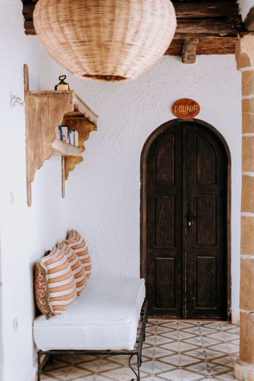 Entrée de l'hôtel Eucalyptus à Essaouira avec porte voûtée en bois foncé, murs blancs et suspension tissée
