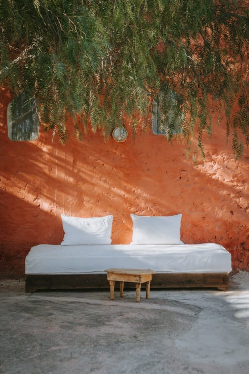 Lit rustique aux draps blancs contre un mur en terre cuite, orné de verdure retombante à l'hôtel Eucalyptus Ethnic à Essaouira, Maroc
