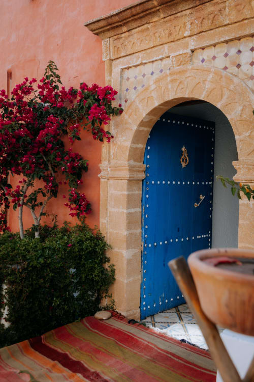 Porte cintrée bleue avec clous en laiton, bougainvillée magenta éclatante et murs en terre cuite à l'Eucalyptus Ethnic Hotel
